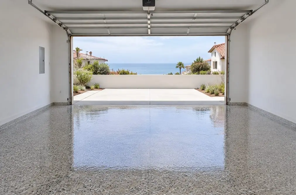 Illustration: a clean two-car Carlsbad garage with a speckled gray, tan and black flake epoxy floor, the garage door open to daylight and no car inside