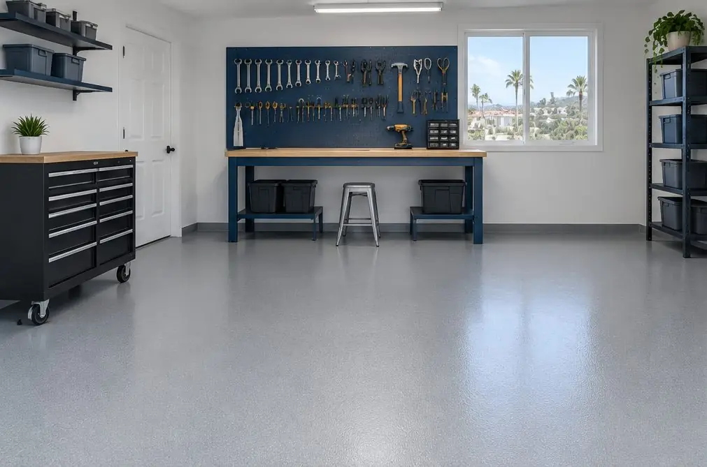 Illustration: a small tidy one-car garage near Carlsbad Village with a smooth light-gray solid-color epoxy floor, a surfboard rack on one wall and a workbench at the back